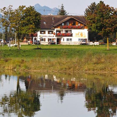 Ferienhaus Gästehaus Stefanie aus der Ferne, gespiegelt im klaren Wasser des Forggensees.